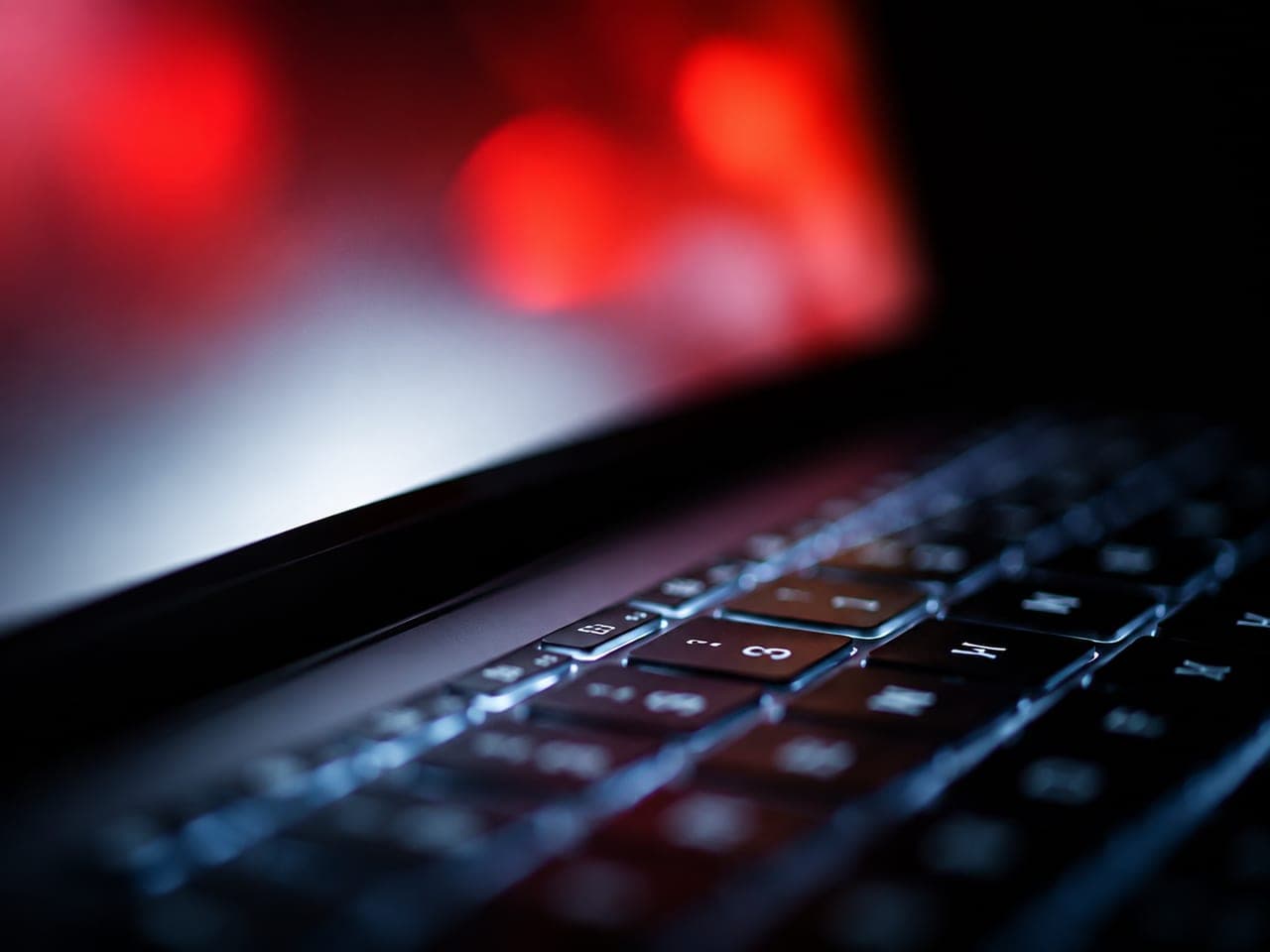 Close-up of a laptop keyboard lit by screen glow at night