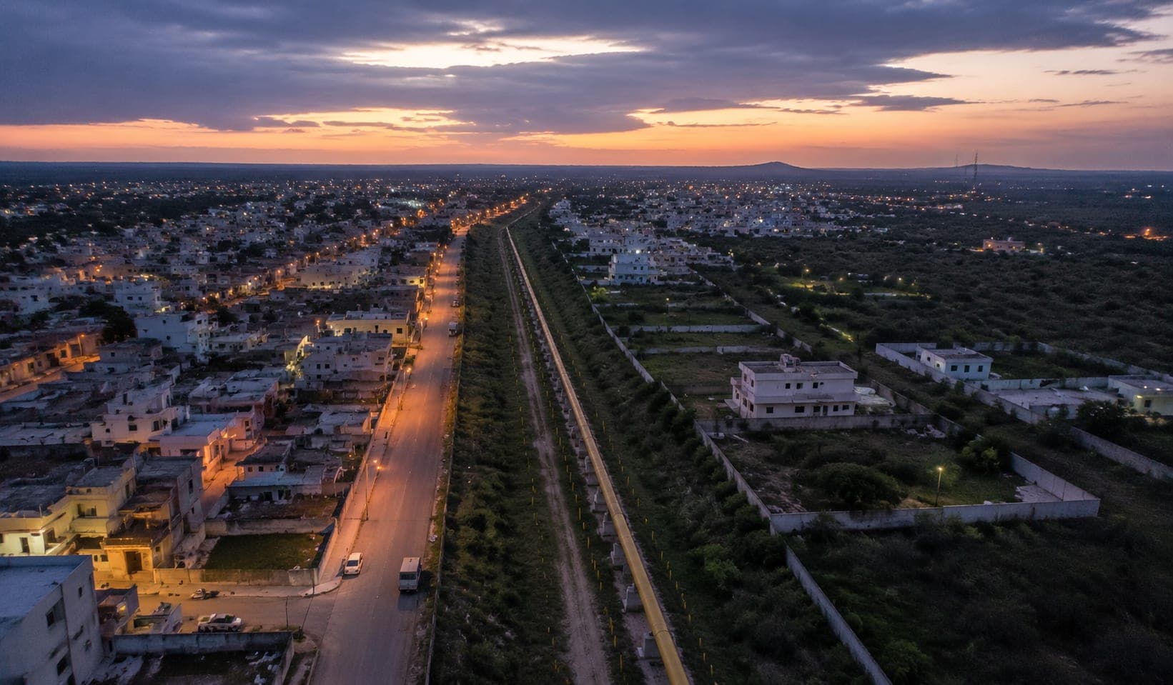 An elevated view of a gas distribution corridor running past a city's outskirts at dusk
